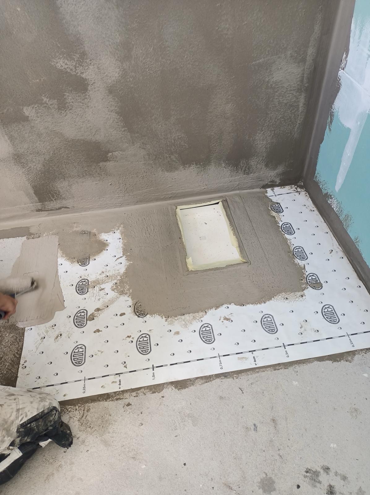 Przygotowanie do hydroizolacji podłogi w łazience w Gorzowie Wielkopolskim: aplikacja masy uszczelniającej wałkiem na folii w płynie marki Ardex, widoczne surowe ściany i wnęka odpływu liniowego.