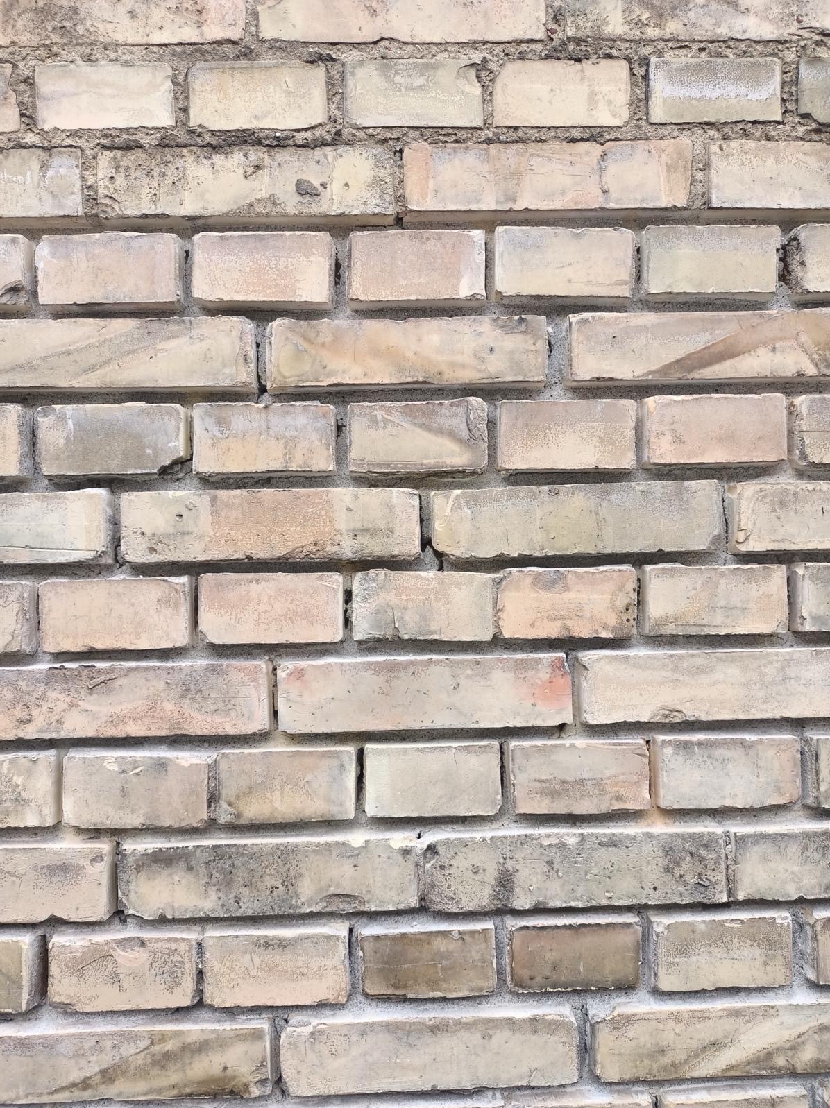 Fragment starej, zabrudzonej ściany z cegły wapienno-piaskowej z widocznymi uszkodzeniami i nierównościami w spoinach.