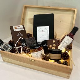 Crazy Fresh - Drewniana skrzynka prezentowa wypełniona kawą, czekoladą, syropem malinowym z imbirem, konfiturą z pigwy, świecą zapachową, czekoladkami Karmello, orzechami, szyszkami i lampkami led, widok z góry.