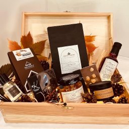 Crazy Fresh - Drewniana skrzynka wypełniona upominkami: kawa, czekolada z migdałami, syrop malinowo-imbirowy, świeca zapachowa o aromacie jabłka i cynamonu, perfumy oraz dekoracyjne szyszki i jesienne liście.