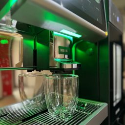 Crazy Fresh - Nowoczesny, podświetlany na zielono ekspres do kawy z dwoma szklankami z podwójnymi ściankami na metalowej tacce ociekowej.