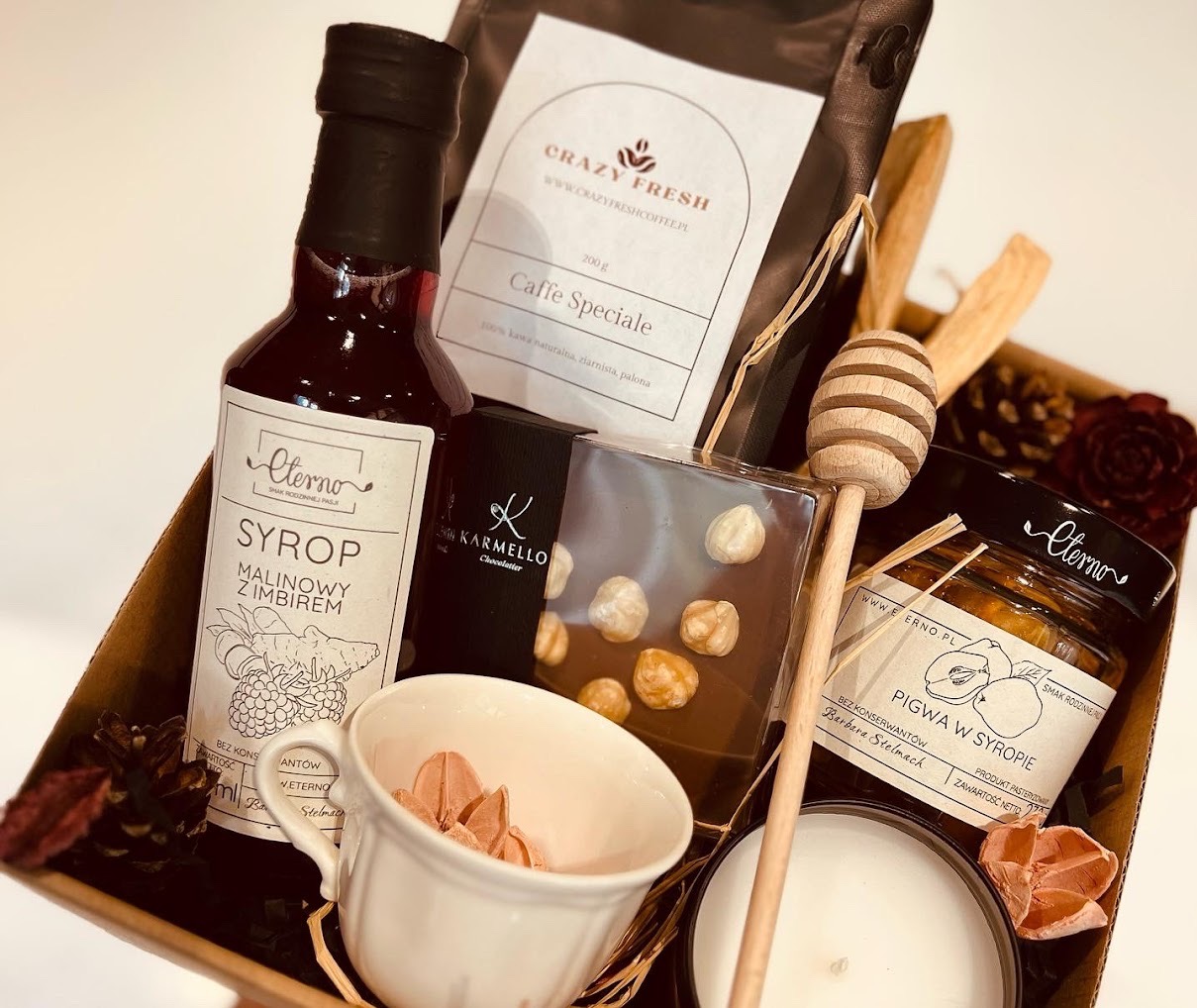 Zestaw prezentowy w kartonowym pudełku: syrop malinowo-imbirowy, czekolada z orzechami, kawa Caffe Speciale, pigwa w syropie, drewniany nabierak do miodu, świeca oraz filiżanka z ozdobnymi...