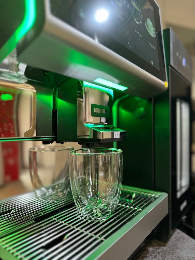 Nowoczesny, podświetlany na zielono ekspres do kawy z dwoma szklankami z podwójnymi ściankami na metalowej tacce ociekowej.