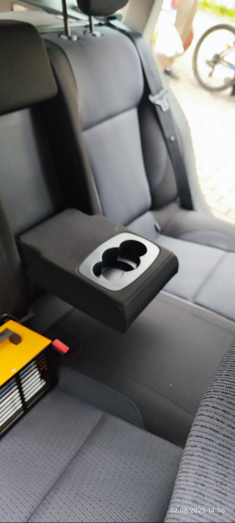 Szare, tylne siedzenie samochodowe z podłokietnikiem i uchwytami na napoje, widoczne narzędzie do czyszczenia. Detailing wnętrza pojazdu.