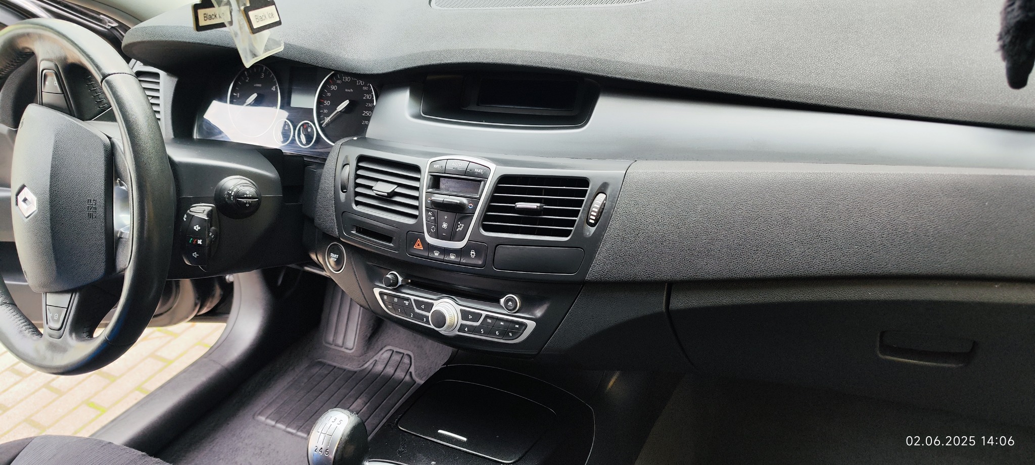 Wnętrze samochodu Renault Laguna, deska rozdzielcza w odcieniach szarości i czerni, widoczna kierownica, panel klimatyzacji i skrzynia biegów. Zapach samochodowy zwisa z lusterka.