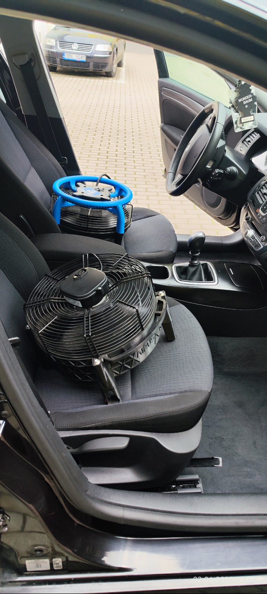 Wnętrze auta z dwoma wentylatorami na siedzeniach, czarny i niebieski, sugerujące przygotowanie do suszenia tapicerki po czyszczeniu.