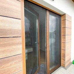 Aurena Marcin Szóstko - Zamknięta i częściowo otwarta plisowana siatka w drewnianej ramie, chroniąca przed owadami, zamontowana na tarasie z drewnianą elewacją.