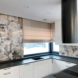 Aurena Marcin Szóstko - Beżowa roleta rzymska w nowoczesnej kuchni z marmurową ścianą, czarnym blatem i białymi szafkami, widok na zasypany śniegiem krajobraz za oknem.