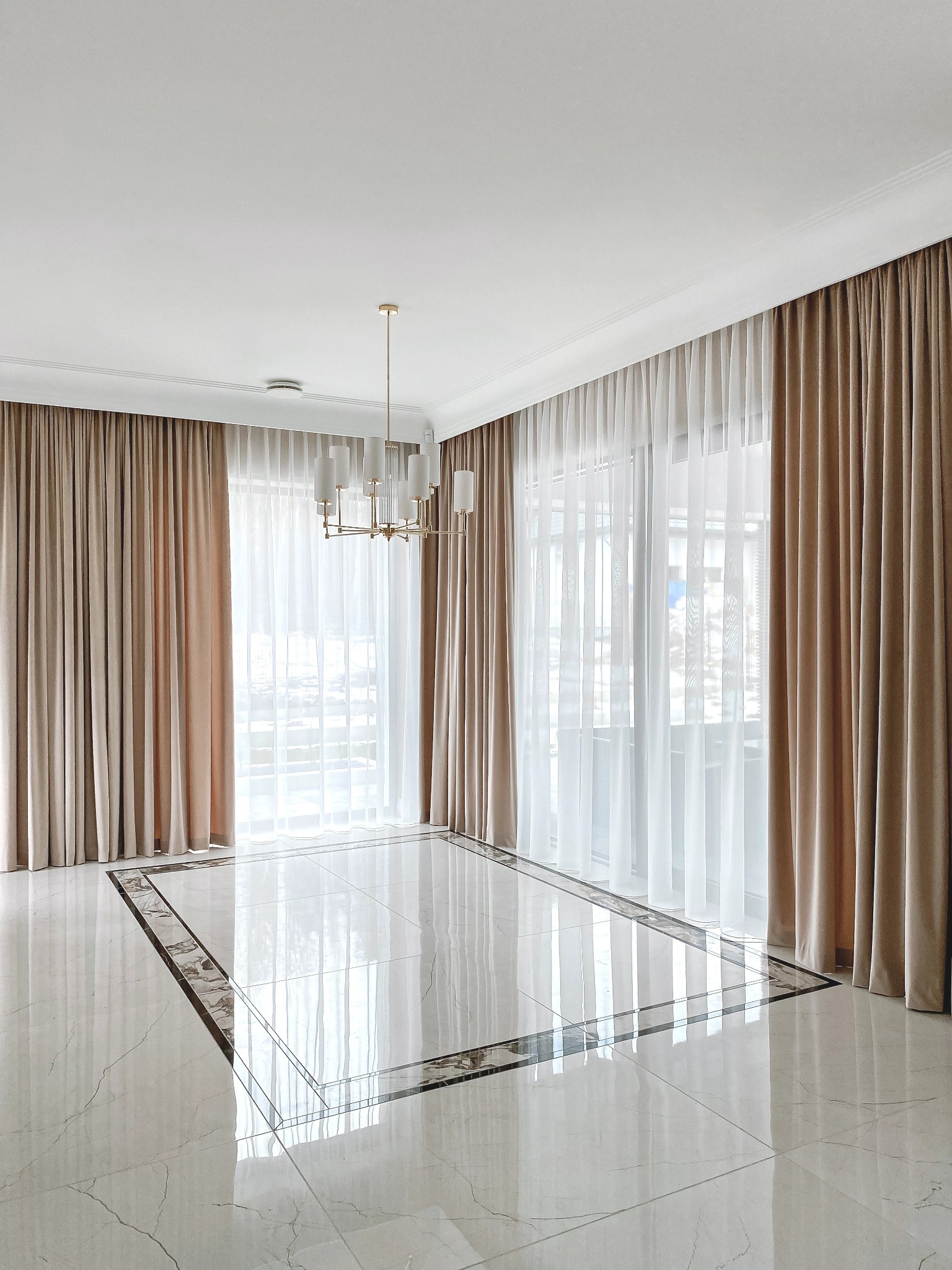 Eleganckie, beżowe zasłony zaciemniające i delikatne, białe firany w przestronnym salonie z marmurową podłogą i złotym żyrandolem.