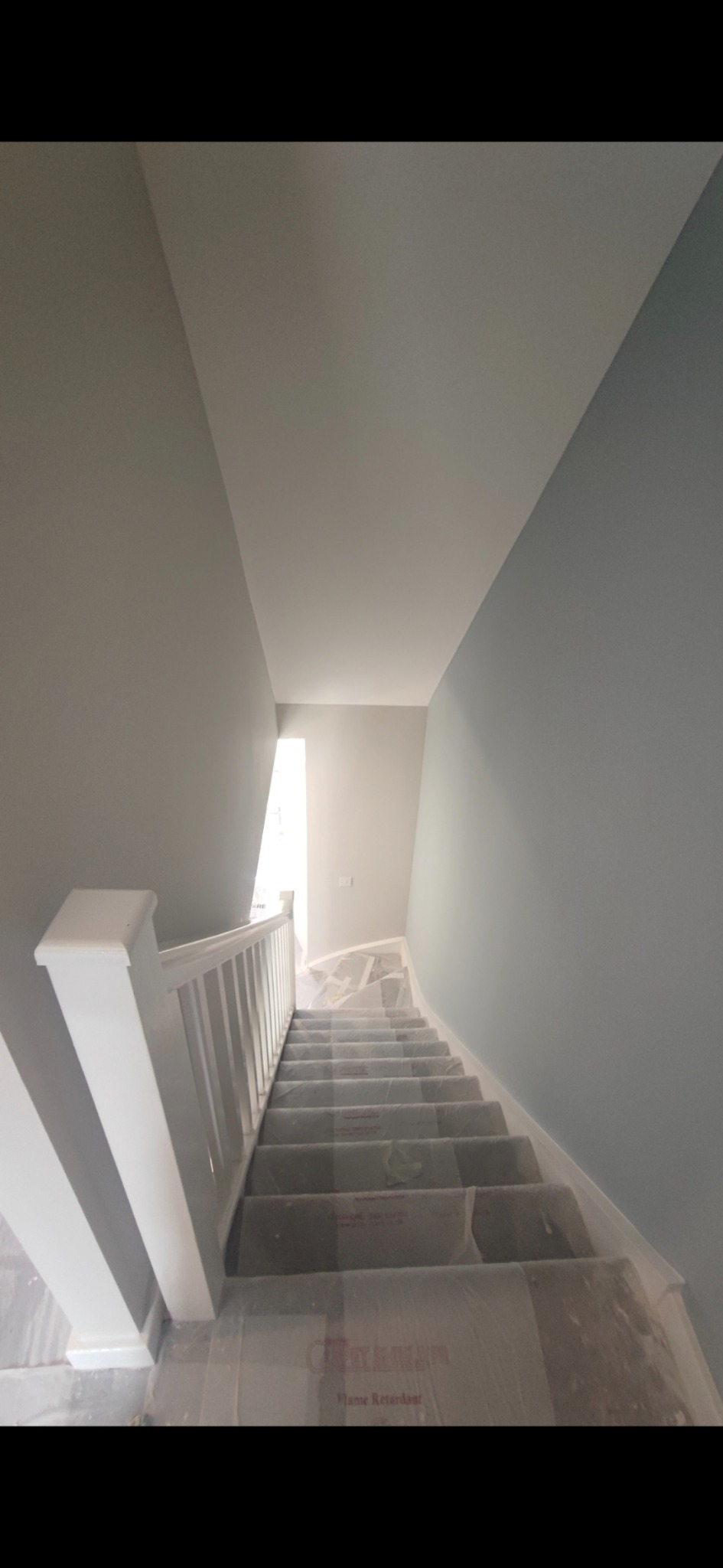 Klatka schodowa w trakcie prac malarskich, zabezpieczone schody folią ochronną, świeżo pomalowane ściany w odcieniach szarości i błękitu.