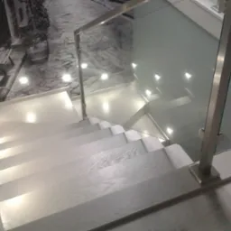 Nowoczesne schody z jasnego drewna z podświetleniem LED w stopniach i szklaną balustradą, widok z g&oacute;ry, na ścianie fototapeta z motywem uliczki.