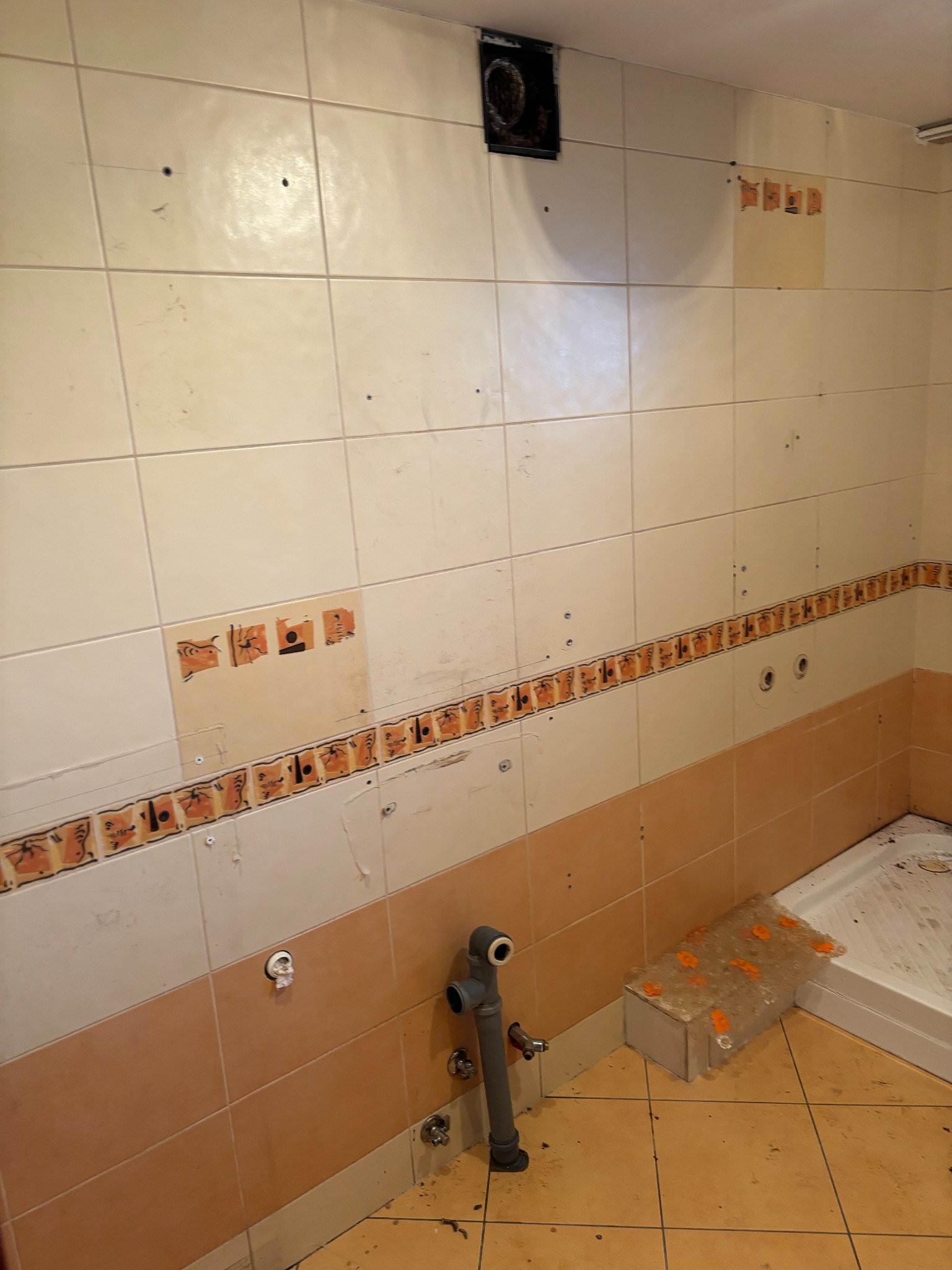 Demontaż starej glazury w łazience, ślady po płytkach na ścianie, widoczne rury i fragment brodzika. Przygotowanie do układania nowych płytek.