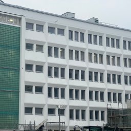 EURO-THERM SPÓŁKA Z OGRANICZONĄ ODPOWIEDZIALNOŚCIĄ - Wielopiętrowy budynek biurowy z białą elewacją, widoczne rusztowania i fragment dźwigu podczas prac budowlanych.