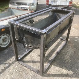 WANDZEL CUSTOM MICHAŁ WANDZEL - Metalowa konstrukcja w trakcie spawania, widoczne spawy na metalowych profilach, w tle przyczepa i dwa samochody.