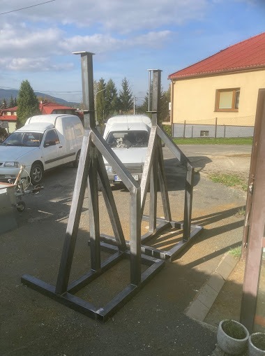 Konstrukcja metalowa spawana, prawdopodobnie szkielet pergoli lub innej konstrukcji ogrodowej, widoczne spawy, tło z budynkiem i samochodami dostawczymi.