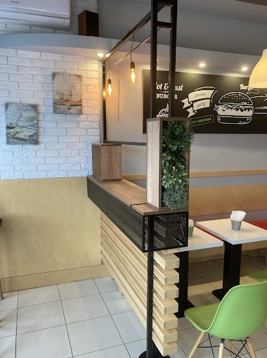 Metalowa konstrukcja z drewnianymi elementami w restauracji, z roślinami w donicach, oświetleniem i grafiką na ścianie w tle.