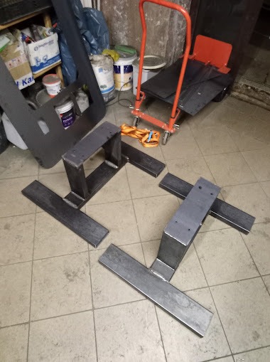 Elementy konstrukcyjne ze stali, prawdopodobnie do balustrady lub schodów, leżące na podłodze warsztatu, widoczne ślady spawania.