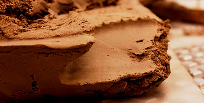 Próbka brązowej, wilgotnej gleby z wyraźną strukturą i krawędzią, leżąca na jasnej, prawdopodobnie kamiennej powierzchni.