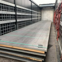 Zaratustra Sp. z o. o. - Stalowe płyty zabezpieczone pasami wewnątrz naczepy ciężarówki, gotowe do transportu. Widoczne kratownice ścian i oświetlenie wewnętrzne.