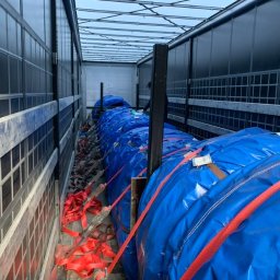 Zaratustra Sp. z o. o. - Ładunek zabezpieczony pasami wewnątrz naczepy. Niebieskie plandeki chronią towar podczas transportu. Widoczne metalowe elementy konstrukcyjne naczepy.
