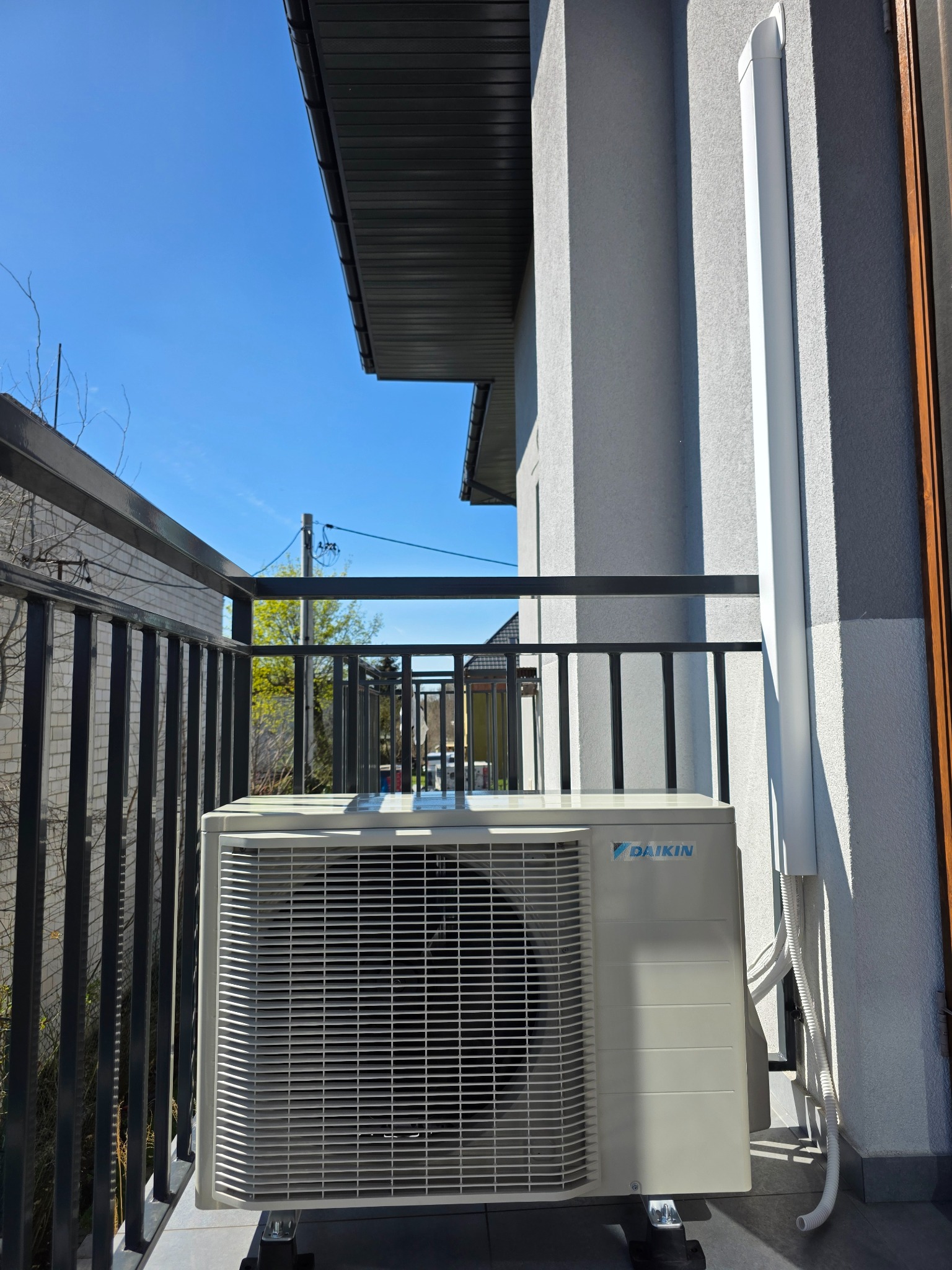 Zewnętrzna jednostka klimatyzacji Daikin zamontowana na balkonie nowoczesnego domu, widoczne czarne barierki i biała elewacja budynku.