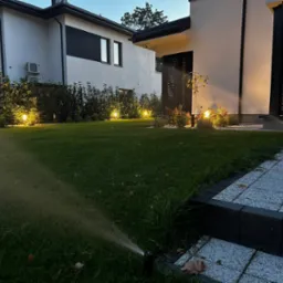 Nowoczesny ogród z automatycznym systemem nawadniania trawnika, oświetleniem punktowym i kostką brukową przy domu.