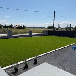 ZIELONA MAGIA MACIEJ STYCZYŃSKI - Świeżo założony trawnik z rolki, widok z góry na równą, zieloną powierzchnię. W tle ogrodzenie panelowe i domy. Fragment tarasu z donicami i niebieski wąż.