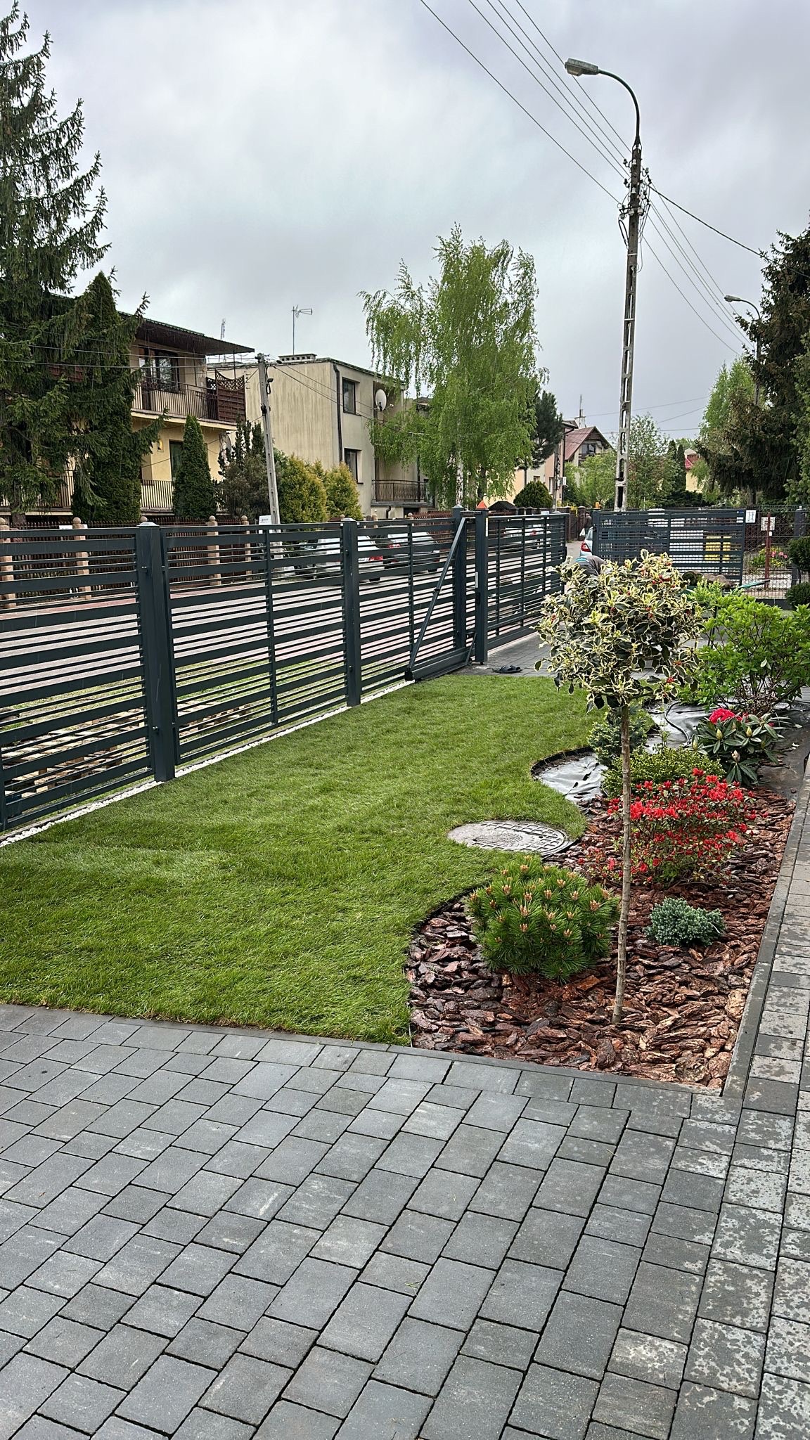 Nowo założony trawnik z rolki, obrzeża wykończone korą, widoczna brama i ogrodzenie posesji.