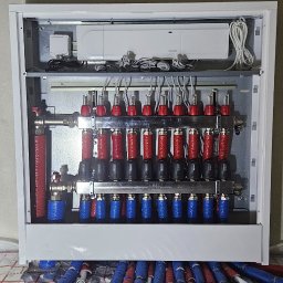 Ciepło pod kontrolą Paweł Kowalczyk - Rozdzielacz ogrzewania podłogowego Uponor w białej szafce, widoczne rury doprowadzające w izolacji czerwono-niebieskiej i sterownik elektroniczny na górze.