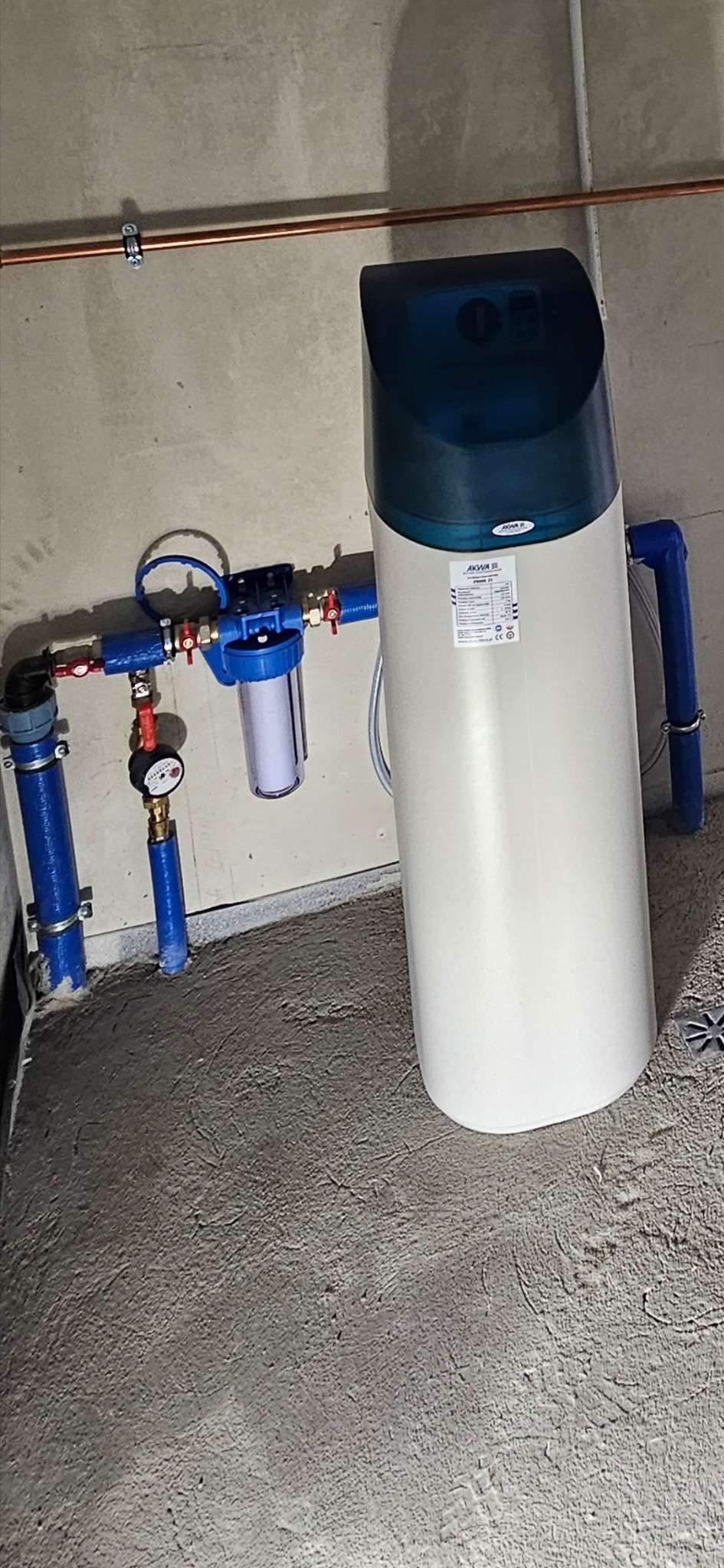 Zamontowany system uzdatniania wody z niebieskimi rurami i manometrem na tle surowego betonu.