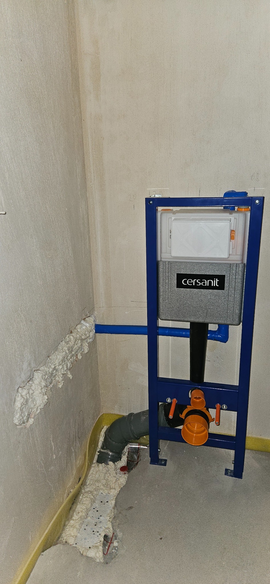 Stelaż podtynkowy Cersanit zamontowany w surowym wnętrzu łazienki, widoczne rury kanalizacyjne i instalacja wodna zabezpieczona pianką montażową.