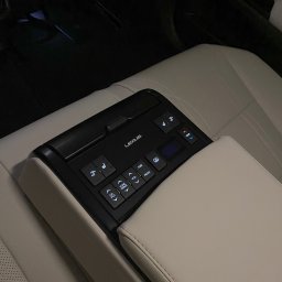 JAKUB PŁATEK LOGISTICS SOLUTIONS - Panel sterowania Lexus z przyciskami do regulacji temperatury, foteli i multimediów, umieszczony w tylnej części pojazdu z beżową skórzaną tapicerką.