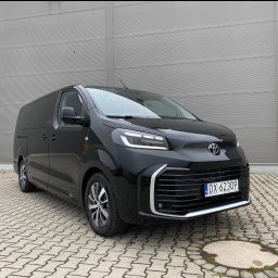 JAKUB PŁATEK LOGISTICS SOLUTIONS - Czarny, nowy Toyota Proace Max z polskimi tablicami na tle szarej ściany. Auto dostawcze, idealne do przewozu osób lub towarów, zaparkowane na kostce brukowej.