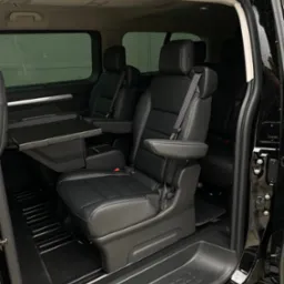 Wnętrze czarnego busa z rozkładanym stolikiem i skórzanymi fotelami. Widok z otwartych drzwi, wnętrze czyste i zadbane, gotowe do komfortowej podróży.