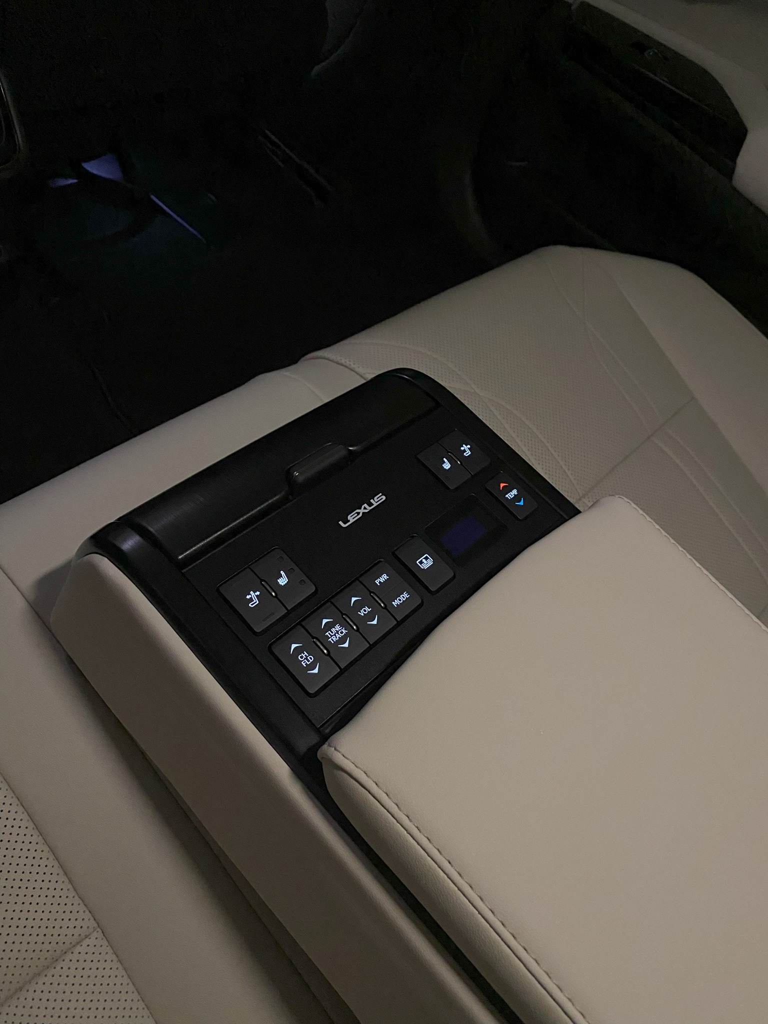 Panel sterowania Lexus z przyciskami do regulacji temperatury, foteli i multimediów, umieszczony w tylnej części pojazdu z beżową skórzaną tapicerką.