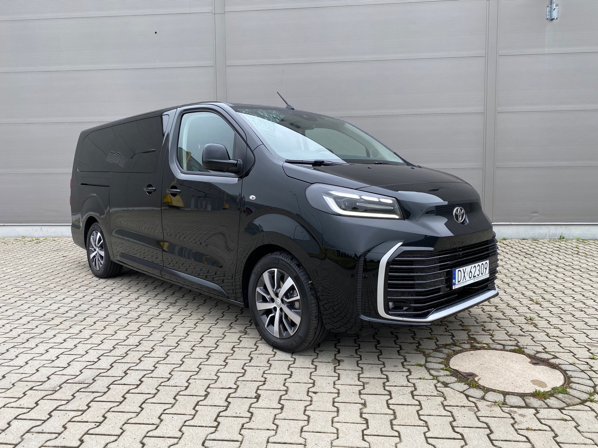 Czarny, nowy bus Toyota Proace Max z tablicą rejestracyjną na tle szarej ściany w Smardach Dolnych. Auto z salonu, gotowe do wynajmu.