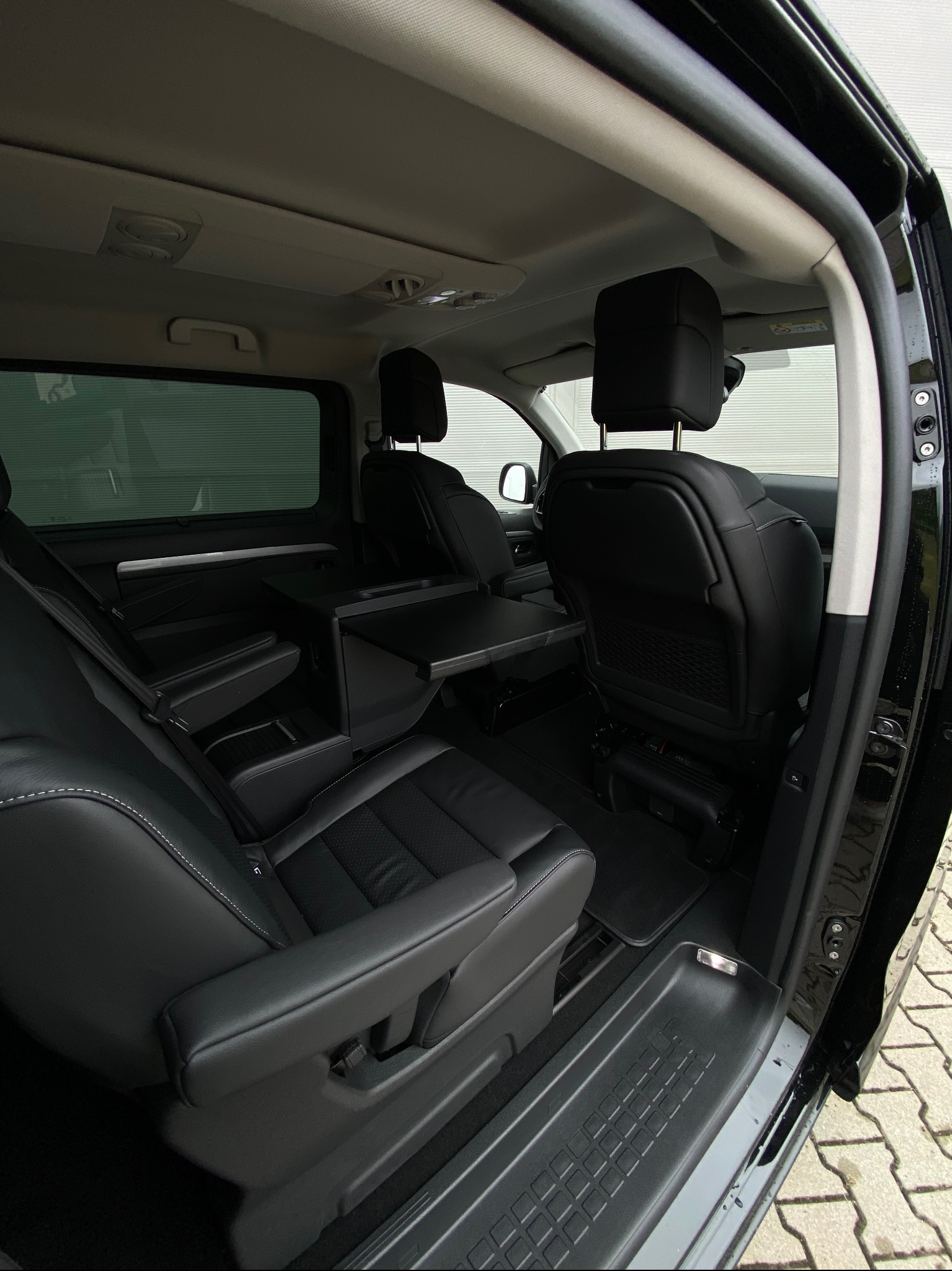 Wnętrze czarnego vana z rozkładanymi stolikami między skórzanymi fotelami. Widok z otwartych drzwi na komfortową przestrzeń pasażerską.