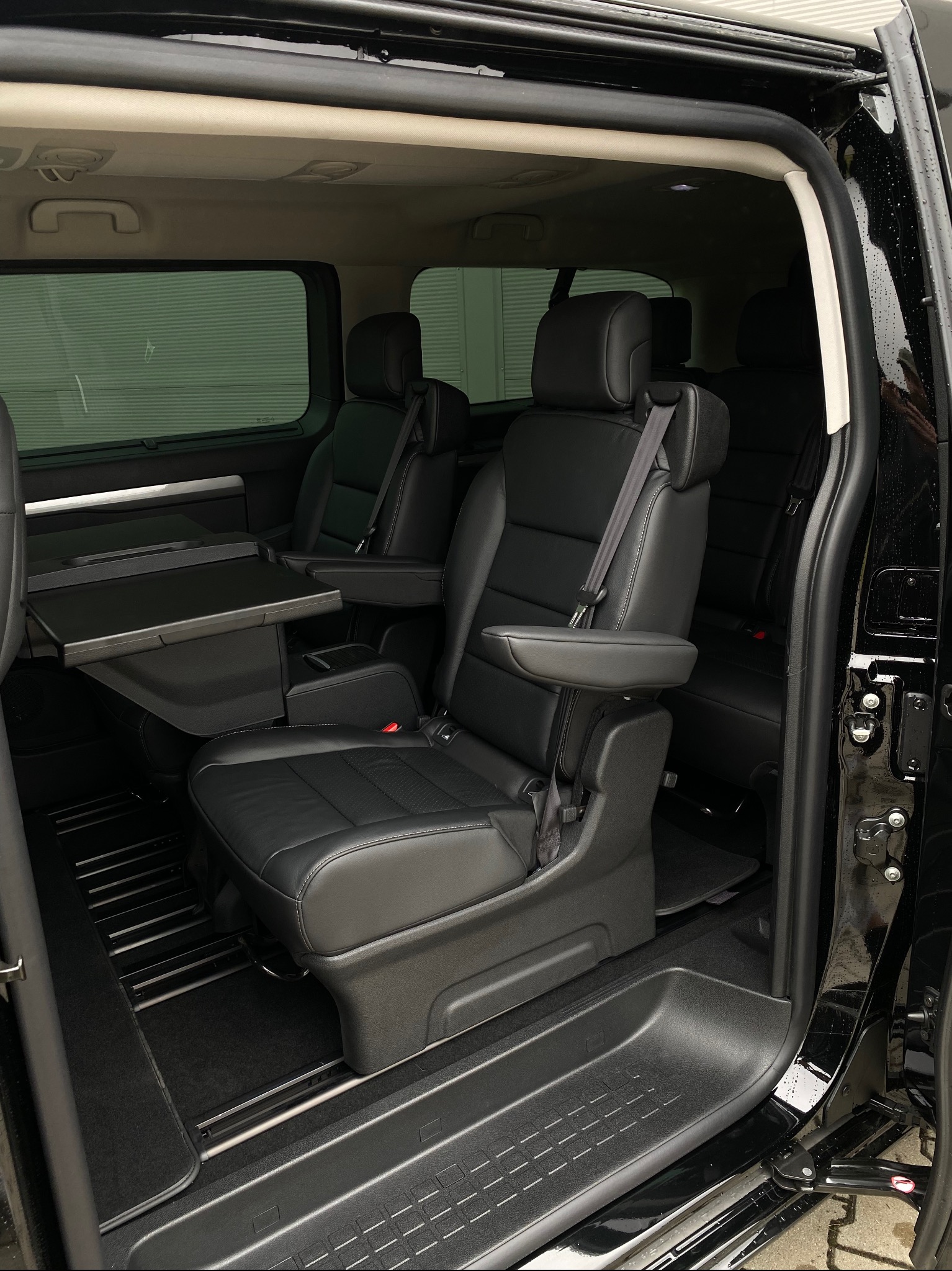 Wnętrze czarnego busa z rozkładanym stolikiem i skórzanymi fotelami. Widok z otwartych drzwi, wnętrze czyste i zadbane, gotowe do komfortowej podróży.