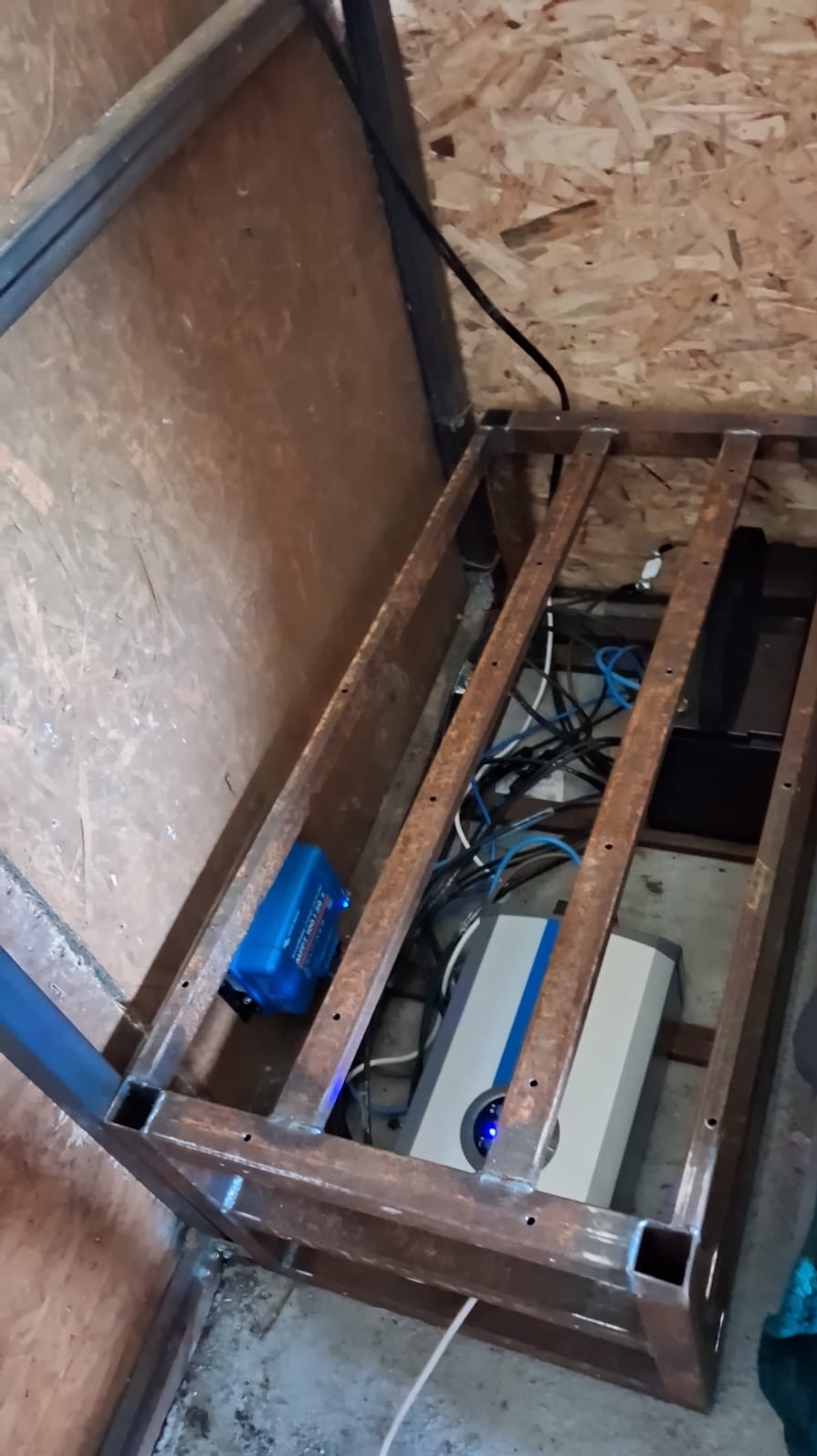 Metalowa rama z osprzętem: inwerter, regulator ładowania i okablowanie. Element instalacji fotowoltaicznej lub magazynu energii w pomieszczeniu gospodarczym.