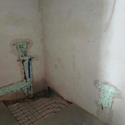 ADMAR INSTALACJE HYDRAULIKA - Instalacja wodna z rurami czerwonymi i niebieskimi w ścianie, uszczelniona pianką, oraz ułożone rury ogrzewania podłogowego na podłodze w pomieszczeniu przed wykończeniem.