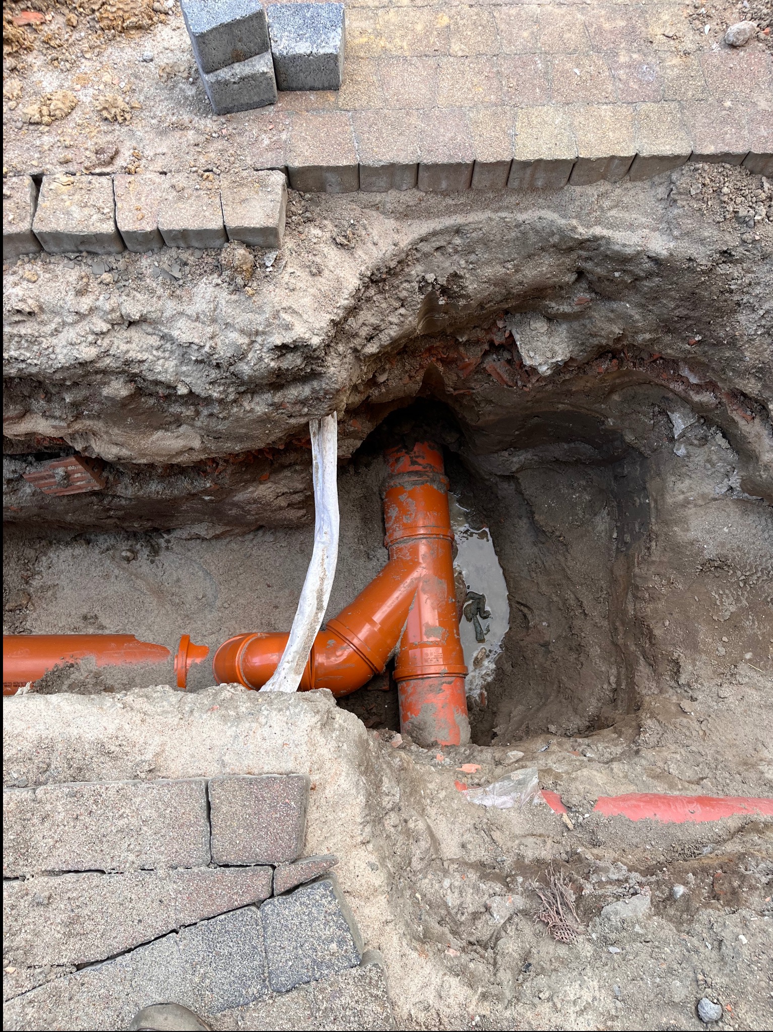 Wykonanie instalacji zewnętrznej: pomarańczowe rury kanalizacyjne w wykopie ziemnym, obok kostki brukowej. Widoczne podejścia wody i stelaż WC w Gowarzewie.