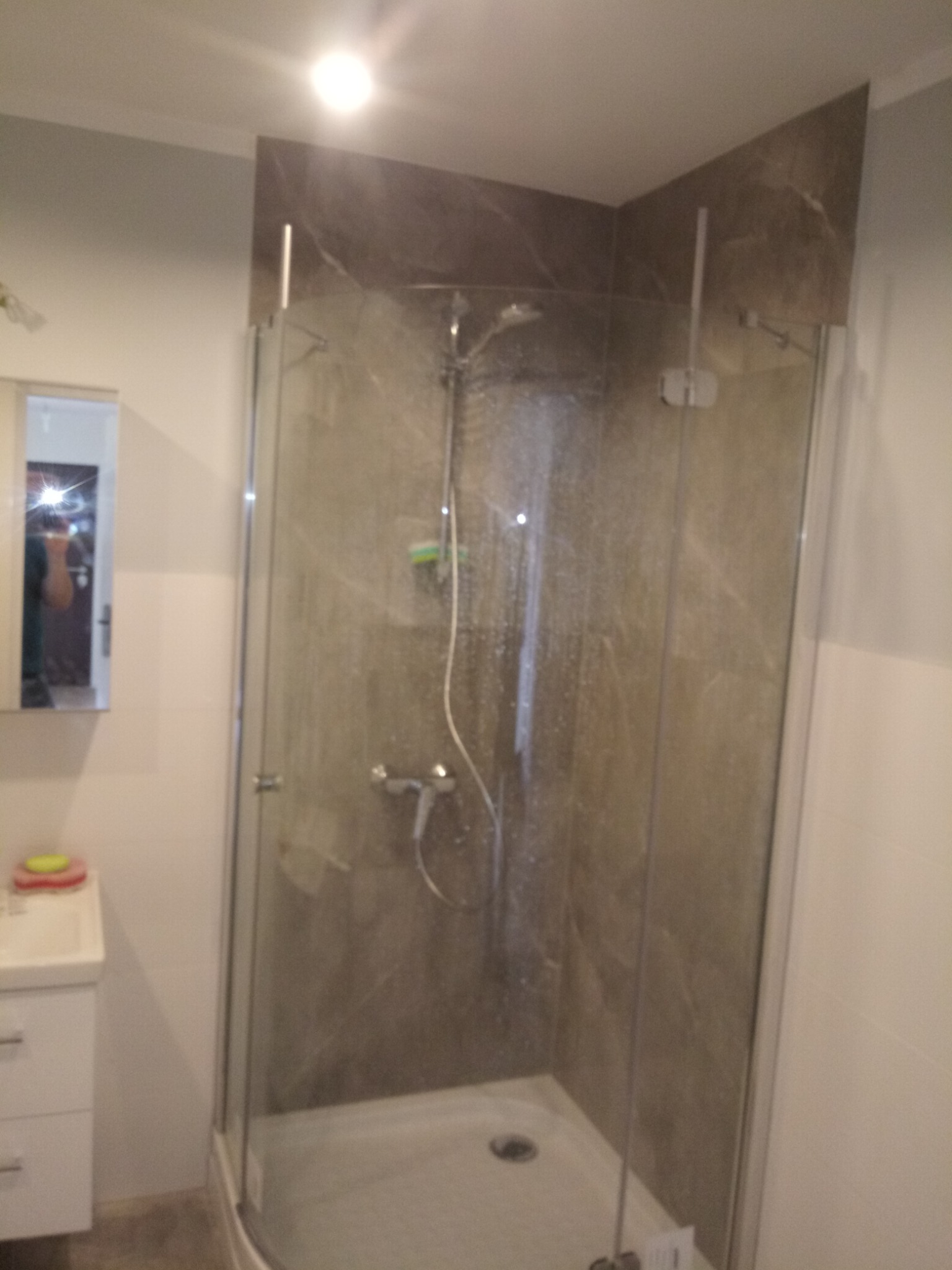 Nowoczesna kabina prysznicowa z szarymi płytkami imitującymi marmur, widoczna również umywalka z szafką i lustro.