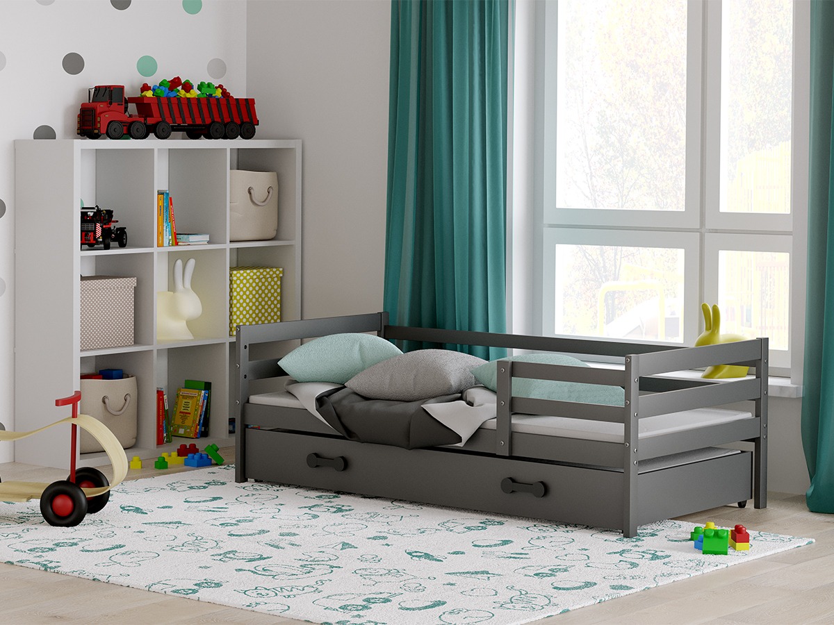 Pokój dziecięcy z szarą, drewnianą sofą-łóżkiem z wysuwanym spaniem, białą półką na zabawki i dywanem w dziecięce wzory, oświetlony naturalnym światłem z okna.