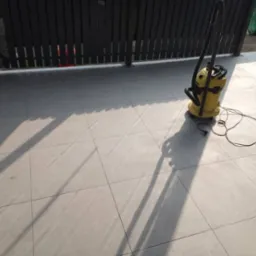 Szare płytki podłogowe na tarasie po umyciu, z żółtym odkurzaczem przemysłowym i widocznymi cieniami.