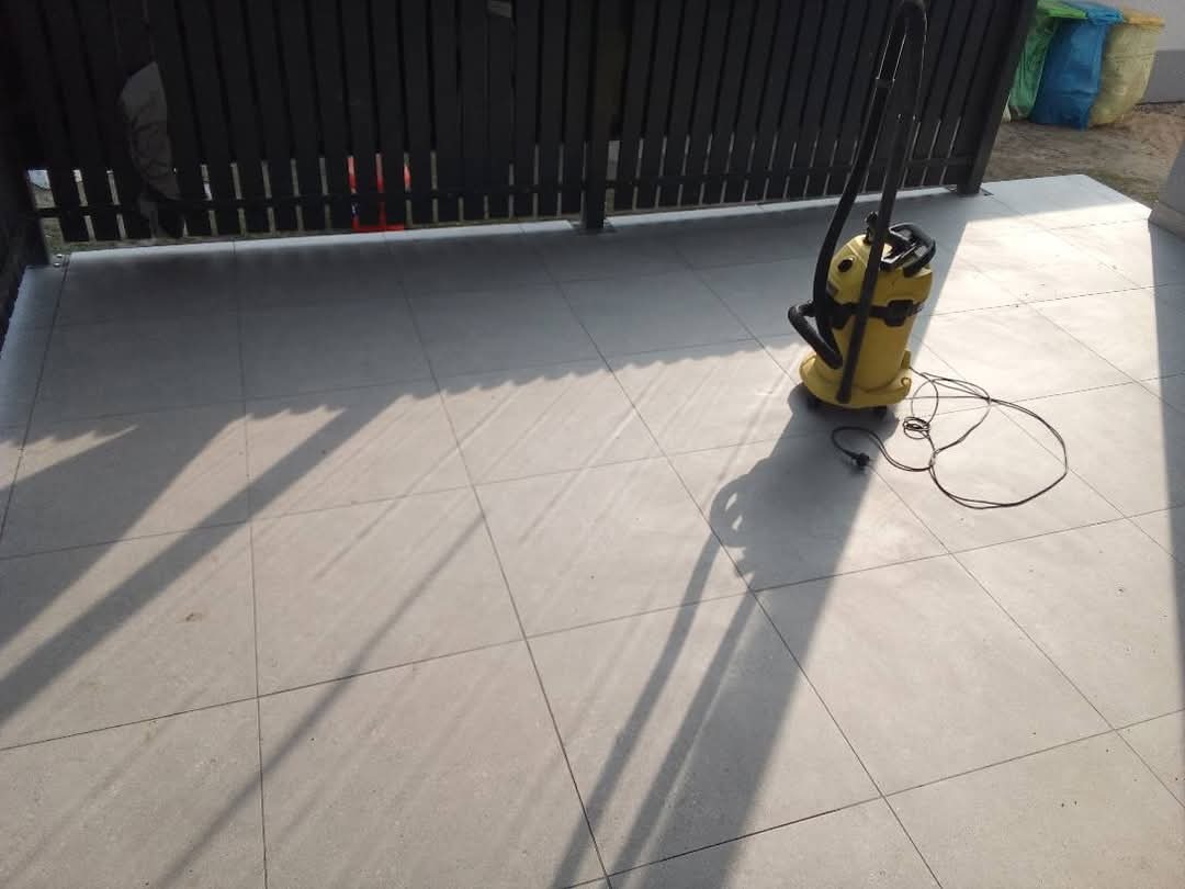 Szare płytki podłogowe na tarasie po umyciu, z żółtym odkurzaczem przemysłowym i widocznymi cieniami.
