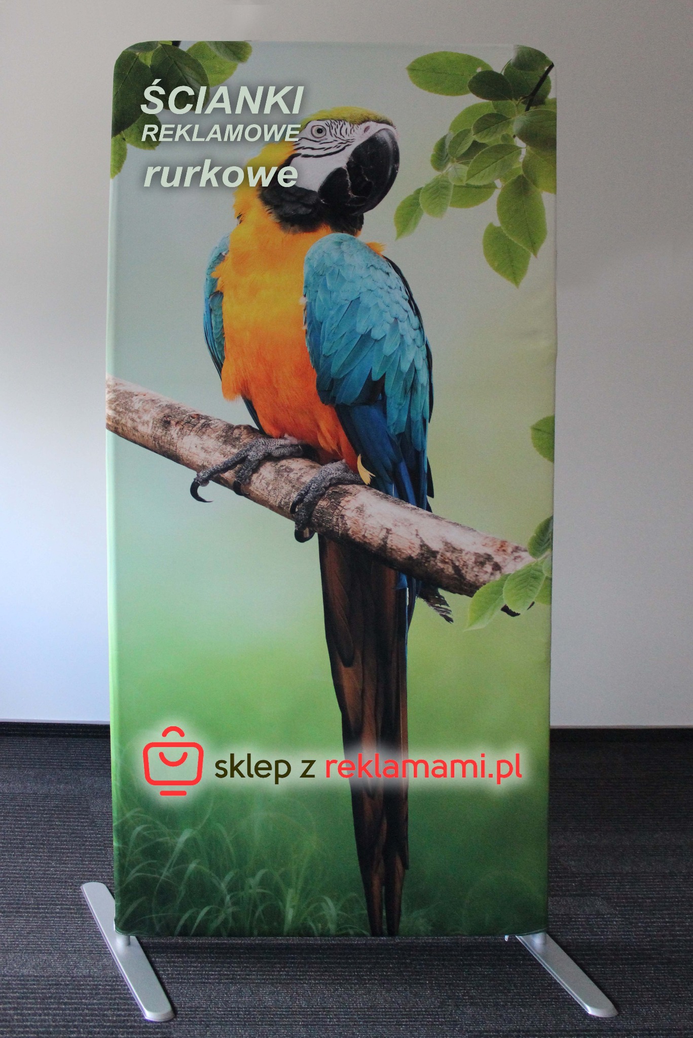 Ścianka reklamowa tekstylna z nadrukiem papugi na gałęzi, w dolnej części logo sklepu internetowego.