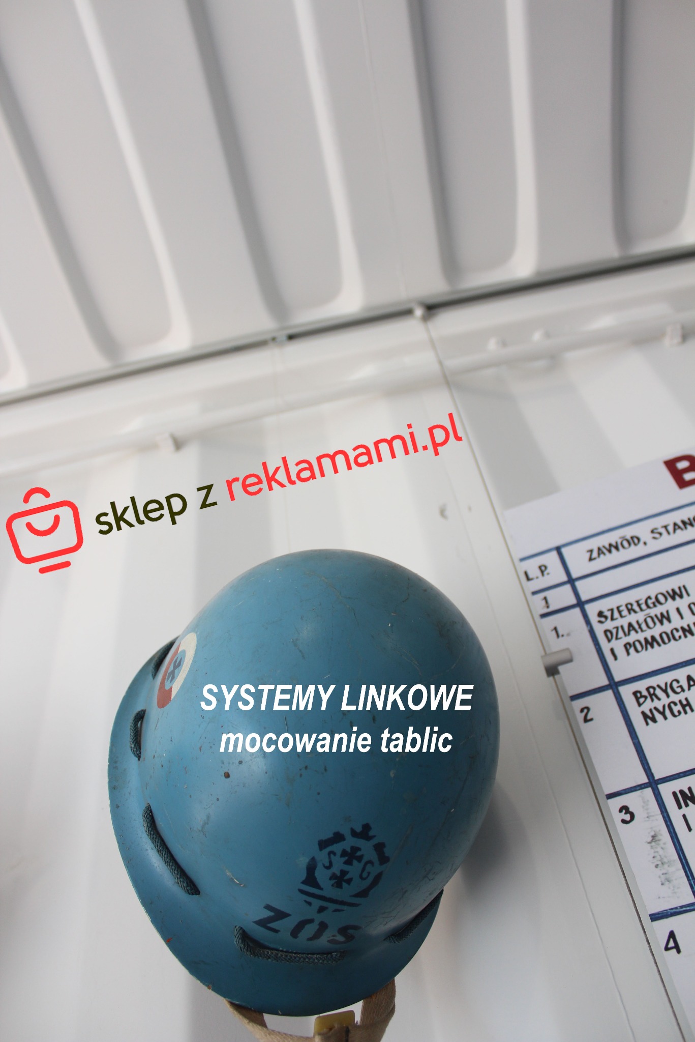 Niebieski hełm z widocznymi systemami linkowymi mocowania tablic, umieszczony obok tablicy z listą zawodów i stanowisk wewnątrz białego kontenera.