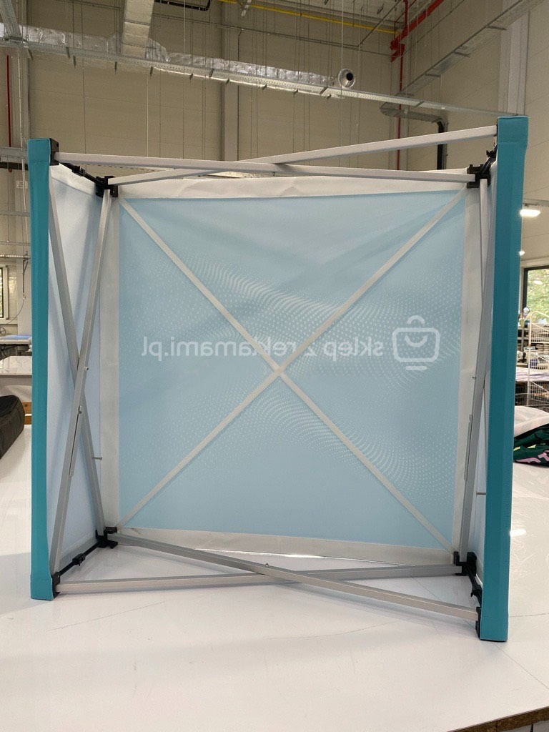 Składana ścianka reklamowa z nadrukiem grafiki w odcieniach błękitu, widoczna konstrukcja aluminiowa i system mocowań, w tle hala produkcyjna.