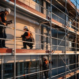 HARDY CONSTRUCTION - Praca na rusztowaniu: czterech robotników w kaskach i kamizelkach montuje elewację budynku. Widok z dołu, ciepłe światło zachodzącego słońca.