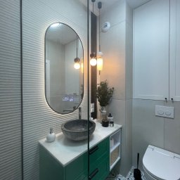 Marta Kieleczawa Project Solutions - Nowoczesna łazienka z umywalką z kamienia, zieloną szafką i podświetlanym lustrem. W tle biała szafka i toaleta. Na podłodze wzorzyste płytki.